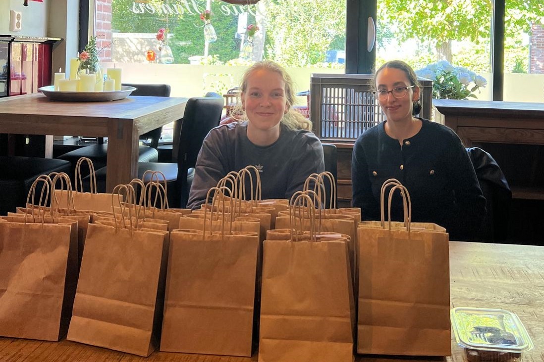 Sociaal werkers Iris Algra en Amal Laghssais van Civic achter een tafel vol goodiebags in café De Drie Hamers in Edam-Volendam.