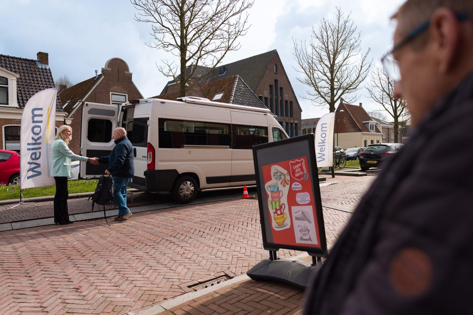 Medewerker dienstverlening Henny van der Wal verwelkomt een bezoeker aan de Landelijke Aangiftedag. Ze staan bij de Belasting-bus. De bus staat geparkeerd voor de Huiskamer van het Leger des Heils in Dokkum.