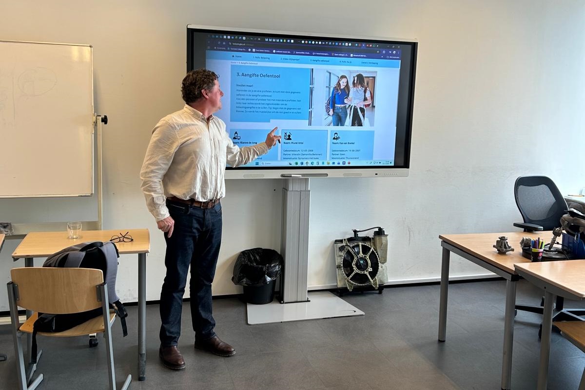André Davidse voor de klas bij PACT Live in Amsterdam. Hij staat voor een scherm. Op het scherm is de Aangifte Oefentool van de Belastingdienst te zien.