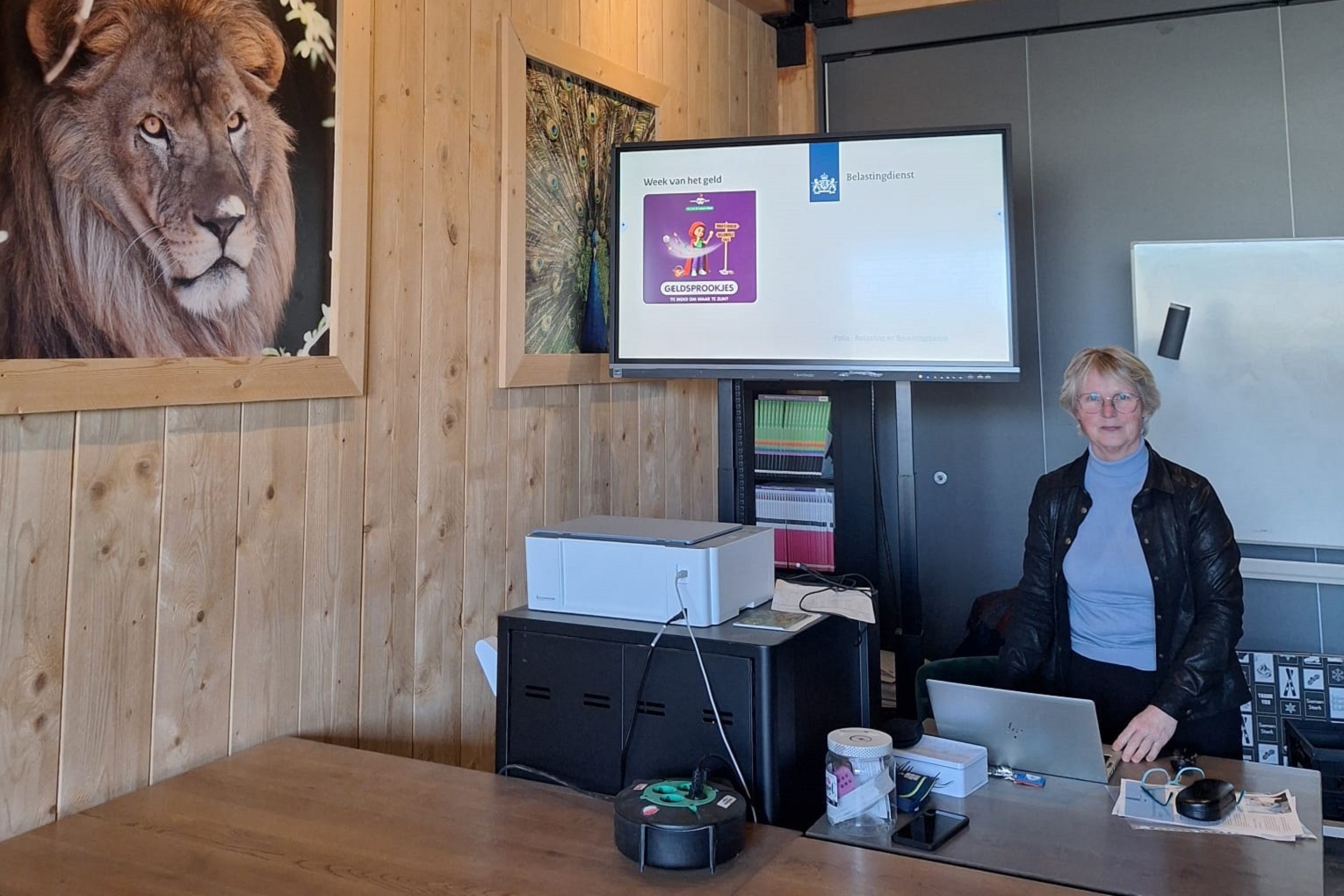 Carla Roelofsen bereidt zich voor op haar gastles. Ze staat voor de klas. Op een groot scherm achter haar is het startscherm te zien van haar presentatie.