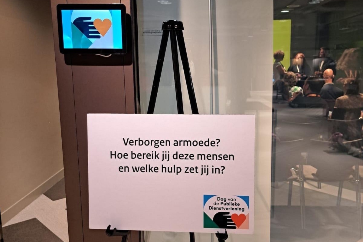 Het bord met de aankondiging van de workshop, voor de deur van de zaal. Op het bord staat: Verborgen armoede? Hoe bereik jij deze mensen en welke hulp zet jij in? Ook het logo van de Dag van de Publieke Dienstverlening staat er op.